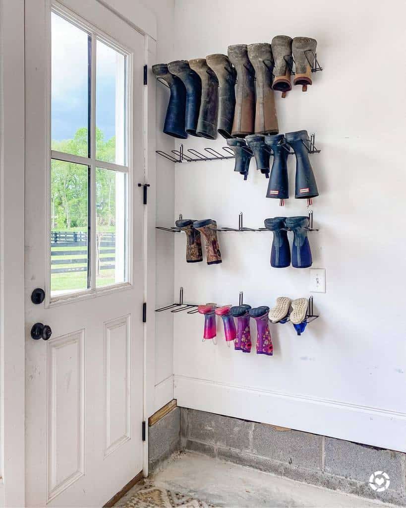 Wall-mounted shoe racks beside a door hold various pairs of boots, including rain boots in different colors and sizes