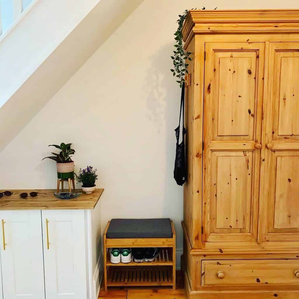 Compact wooden shoe bench with a cushioned seat and slatted storage, placed in a cozy hallway corner with natural wood furniture