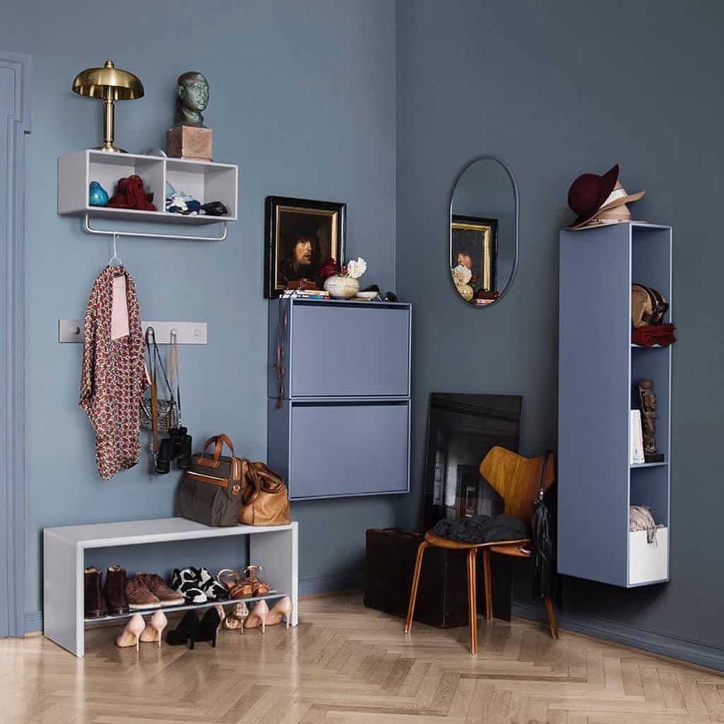 A stylish entryway with blue walls, shelves, a mirror, shoes, bags, hats, and framed art; warm wooden flooring adds contrast