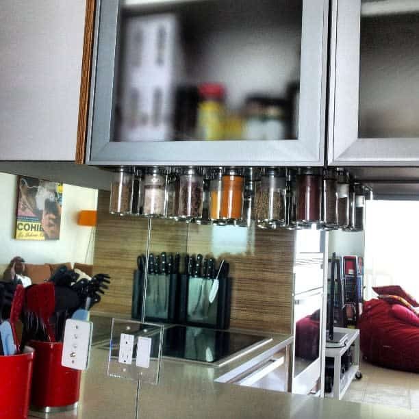 A modern kitchen with spice jars under a cabinet, knives in a block on the counter, and a blurred poster on the wall