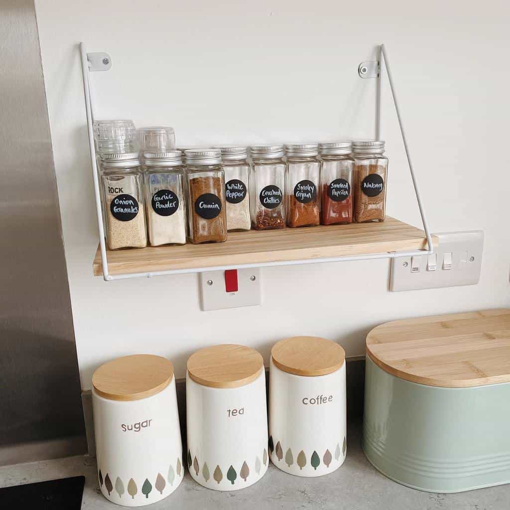 Minimalist hanging spice shelf with labeled glass jars, paired with matching tea, coffee, and sugar canisters for a clean and organized kitchen