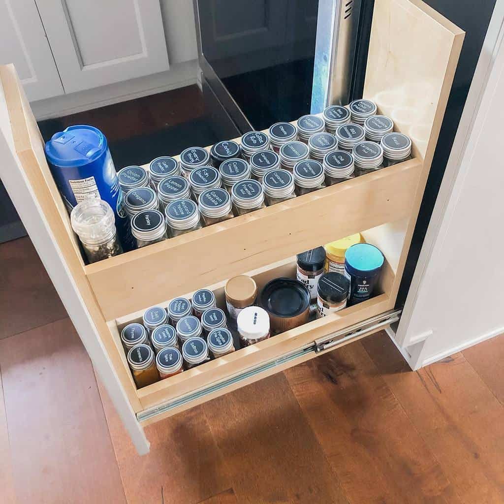 Pull-out kitchen drawer with organized spice jars and containers arranged neatly in two rows