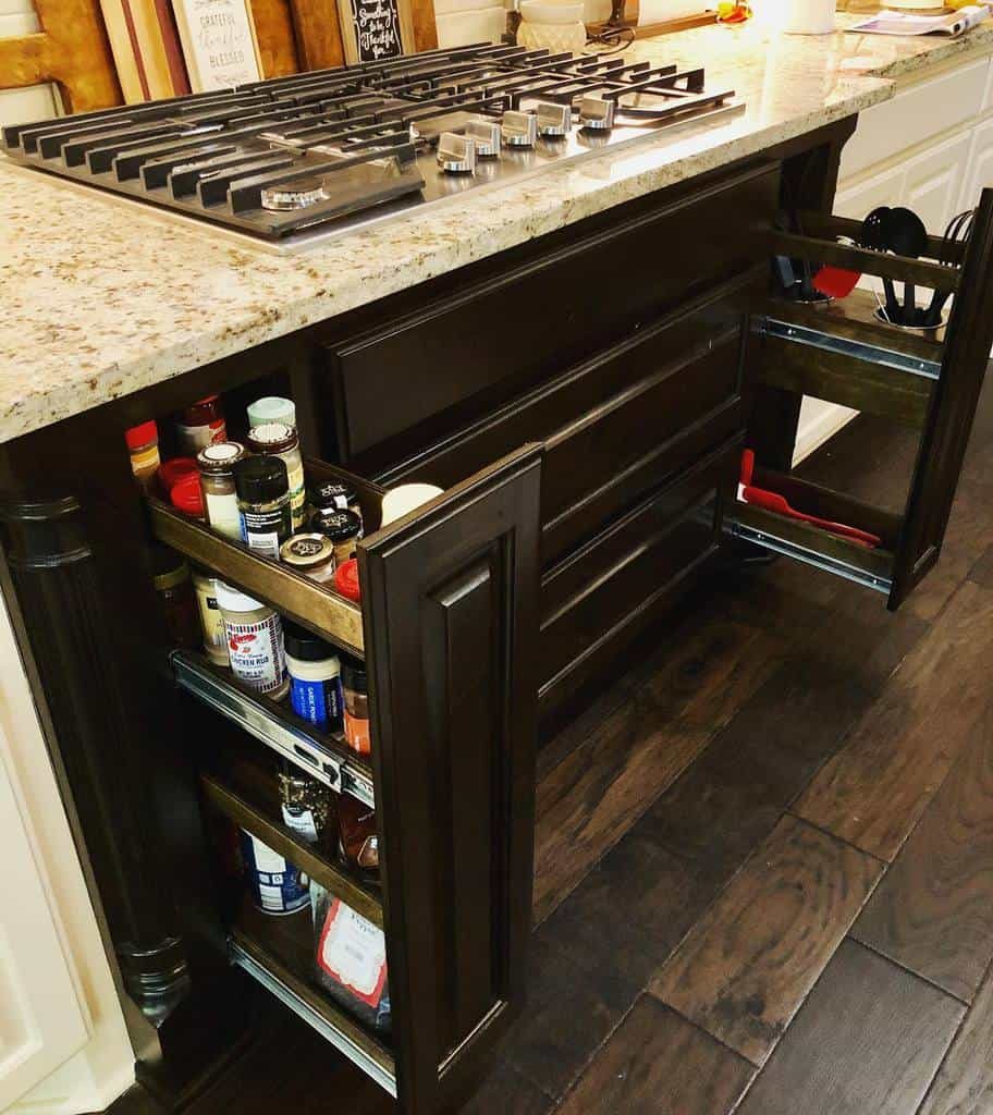 Kitchen island with gas stove and pull-out spice racks on both sides, set against dark wood cabinetry and a granite countertop