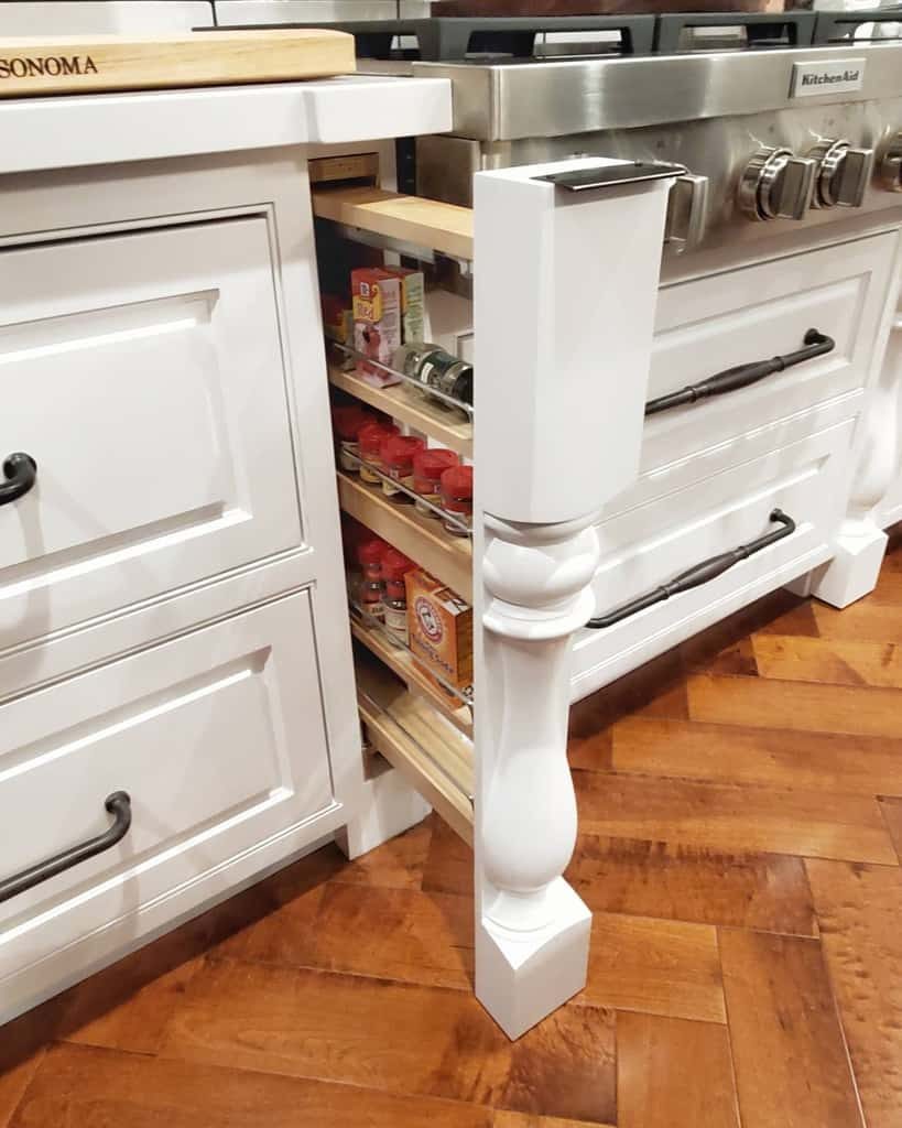 A kitchen with a pull-out spice rack hidden between a cabinet and an oven, displaying various spices