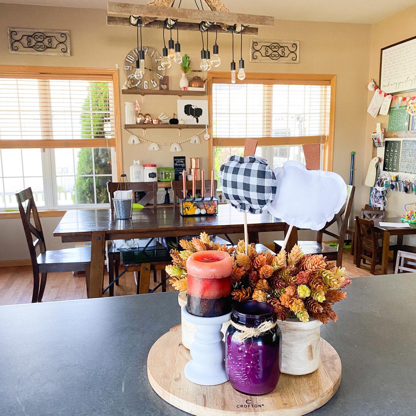 Cozy kitchen with a fall-themed centerpiece on a round tray, featuring candles, flowers, and decorative apples