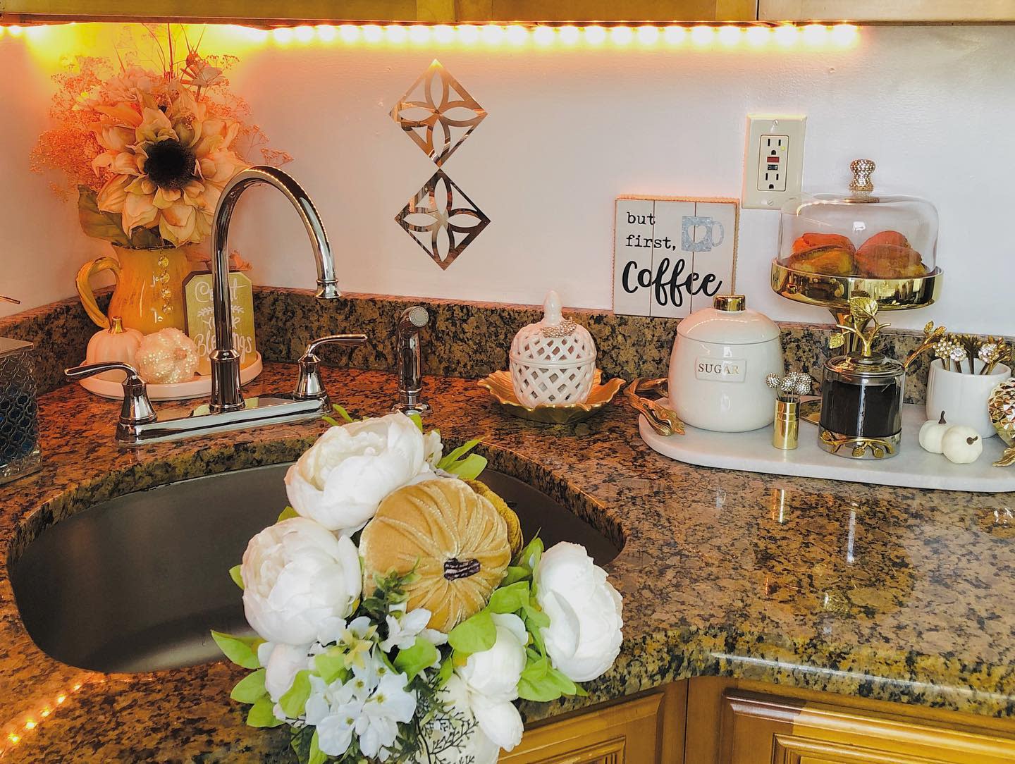 Cozy fall-themed kitchen decor with flowers, pumpkins, a cake stand with pastries, and a coffee sign on a granite countertop