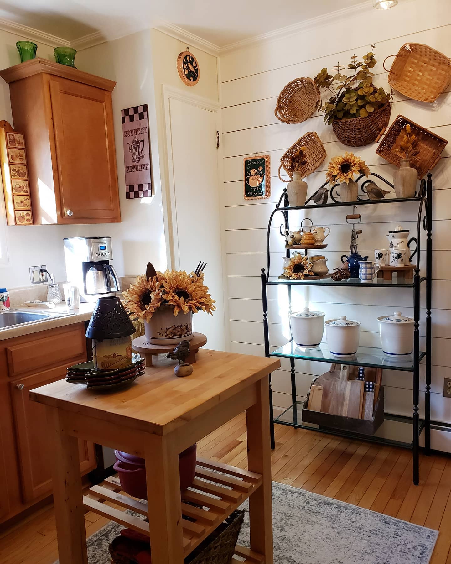 A cozy kitchen with wooden cabinetry, a small island, and shelves decorated with baskets