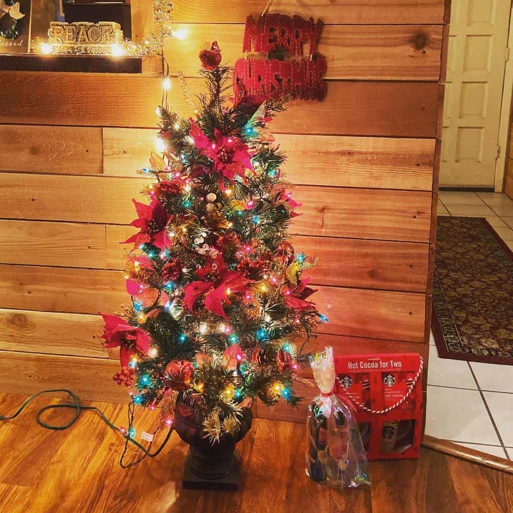 Small Christmas tree with colorful lights and red decorations, set against a wooden wall