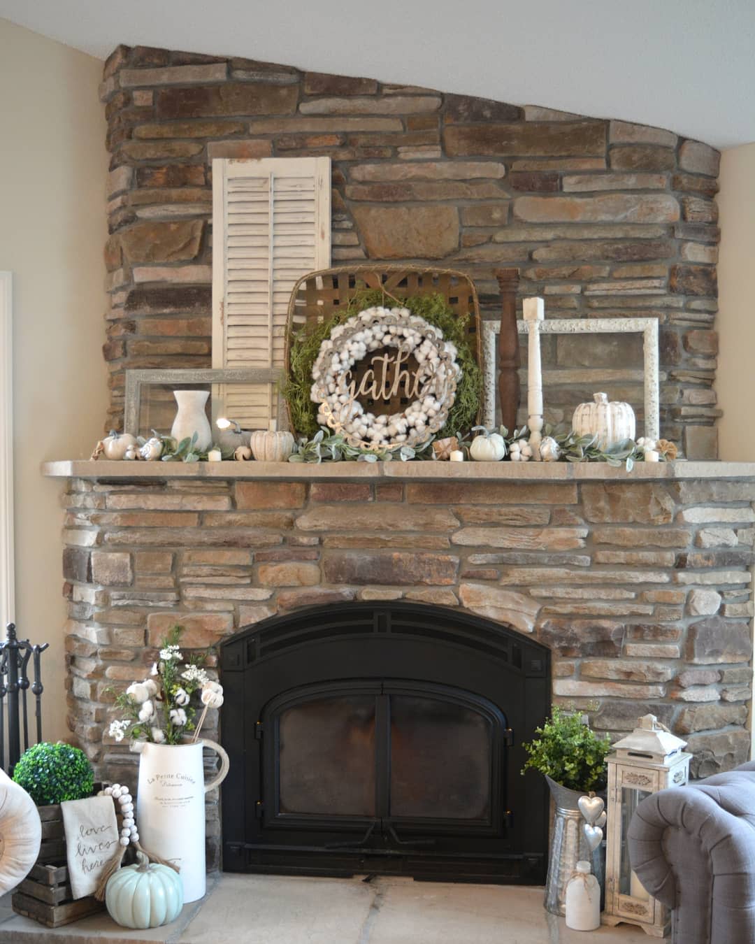 Stone fireplace with fall decor, including a cotton wreath, pumpkins, foliage, lanterns, and a rustic "gather" sign on the mantel