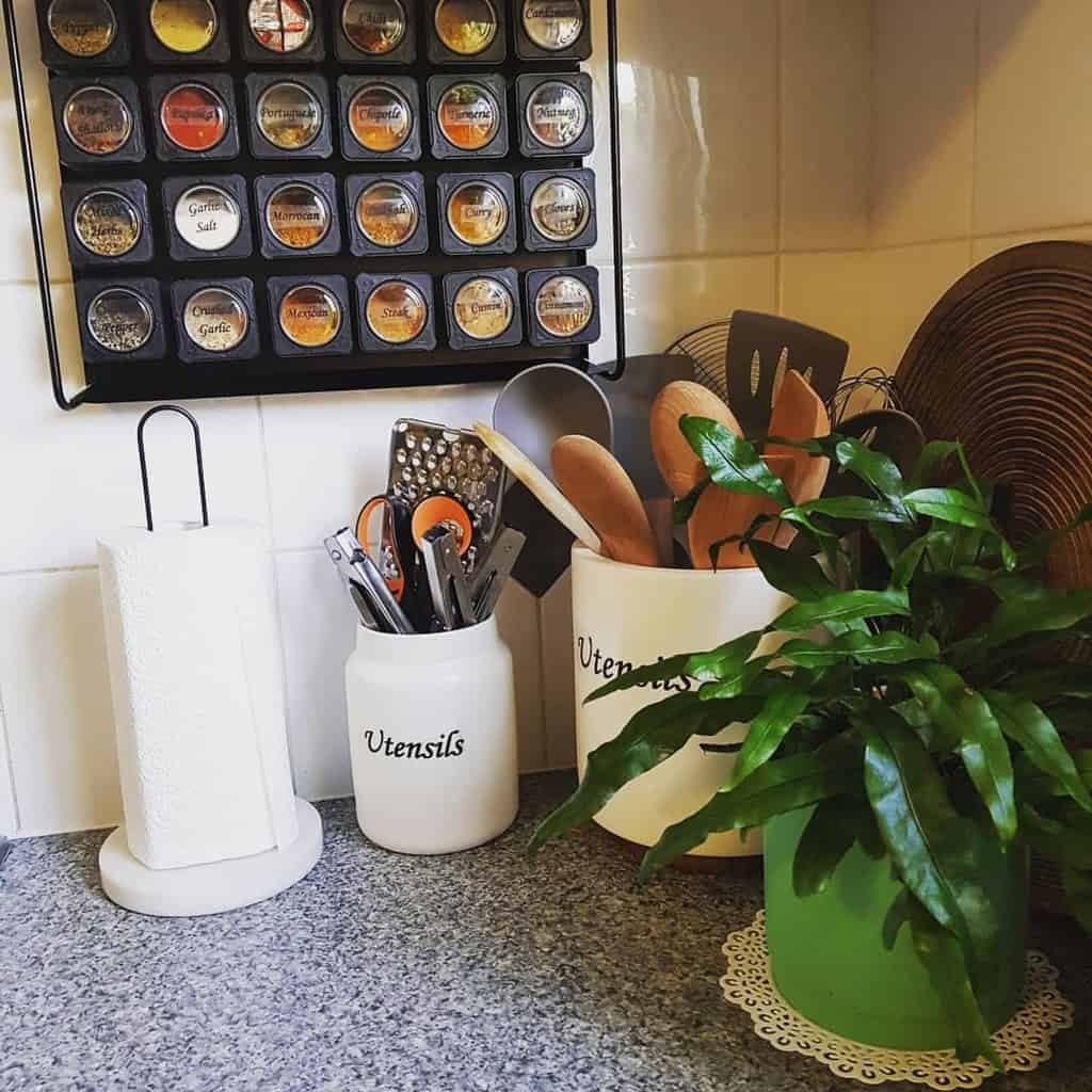 Wall-mounted magnetic spice rack with labeled jars, complementing a neatly organized kitchen countertop with utensils and greenery