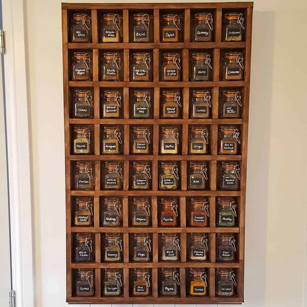 Wall-mounted spice rack with labeled glass jars, each containing a different spice, organized in a wooden grid