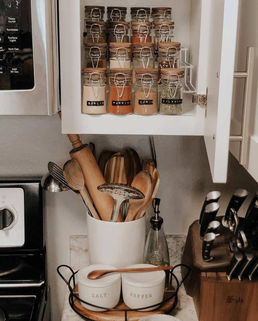 Kitchen corner with spice jars in a cabinet, utensils in a holder, and salt and pepper bowls on the counter, knife block nearby