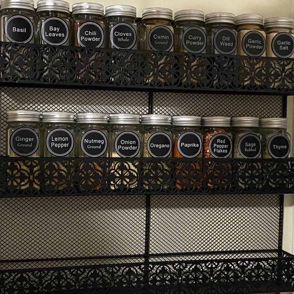 A metal spice rack holding jars labeled with various spices, such as basil, chili powder, oregano, and thyme