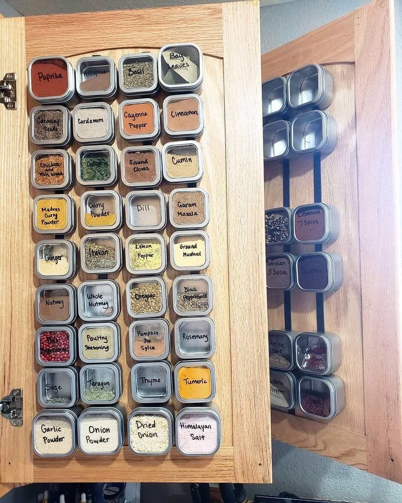 Wooden spice rack with various labeled spices in metal tins, attached inside a cabinet door