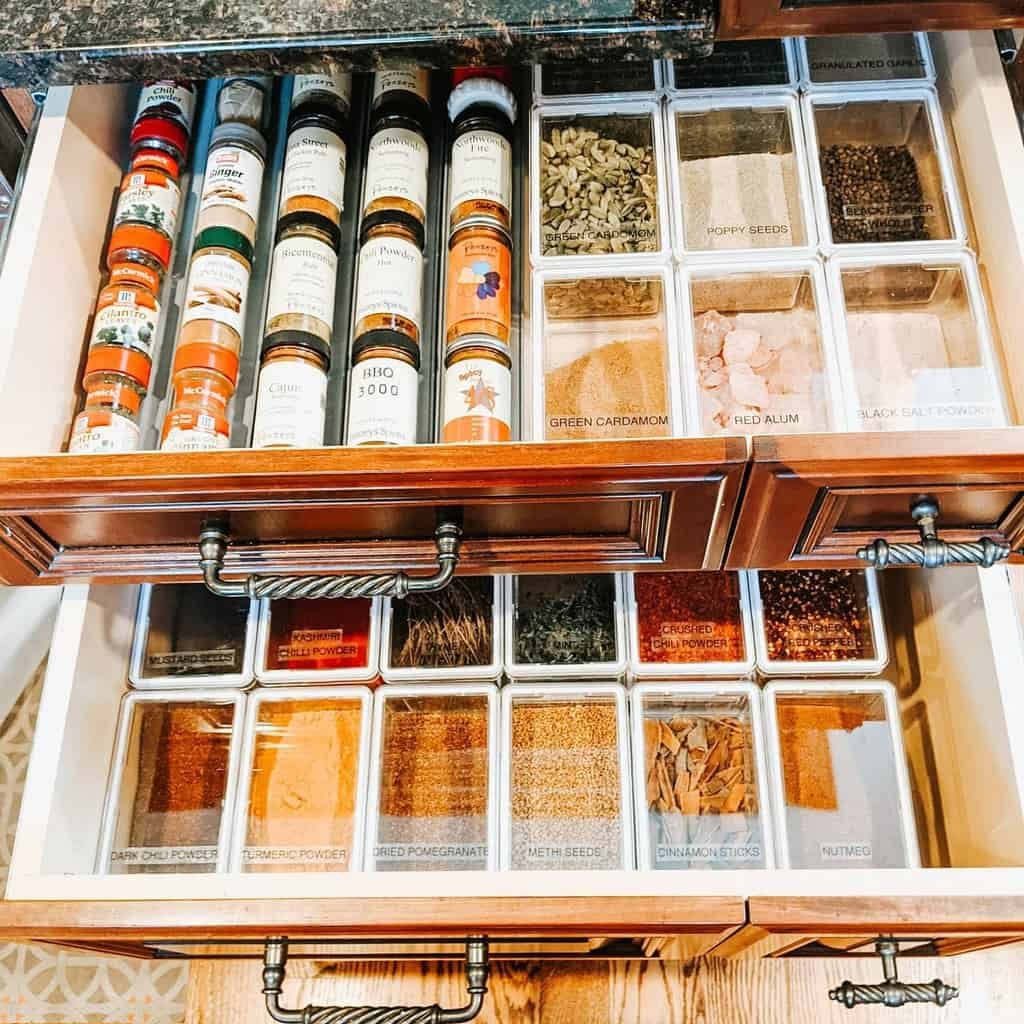 Open spice drawer with neatly organized jars and labeled sections containing various spices and seasonings