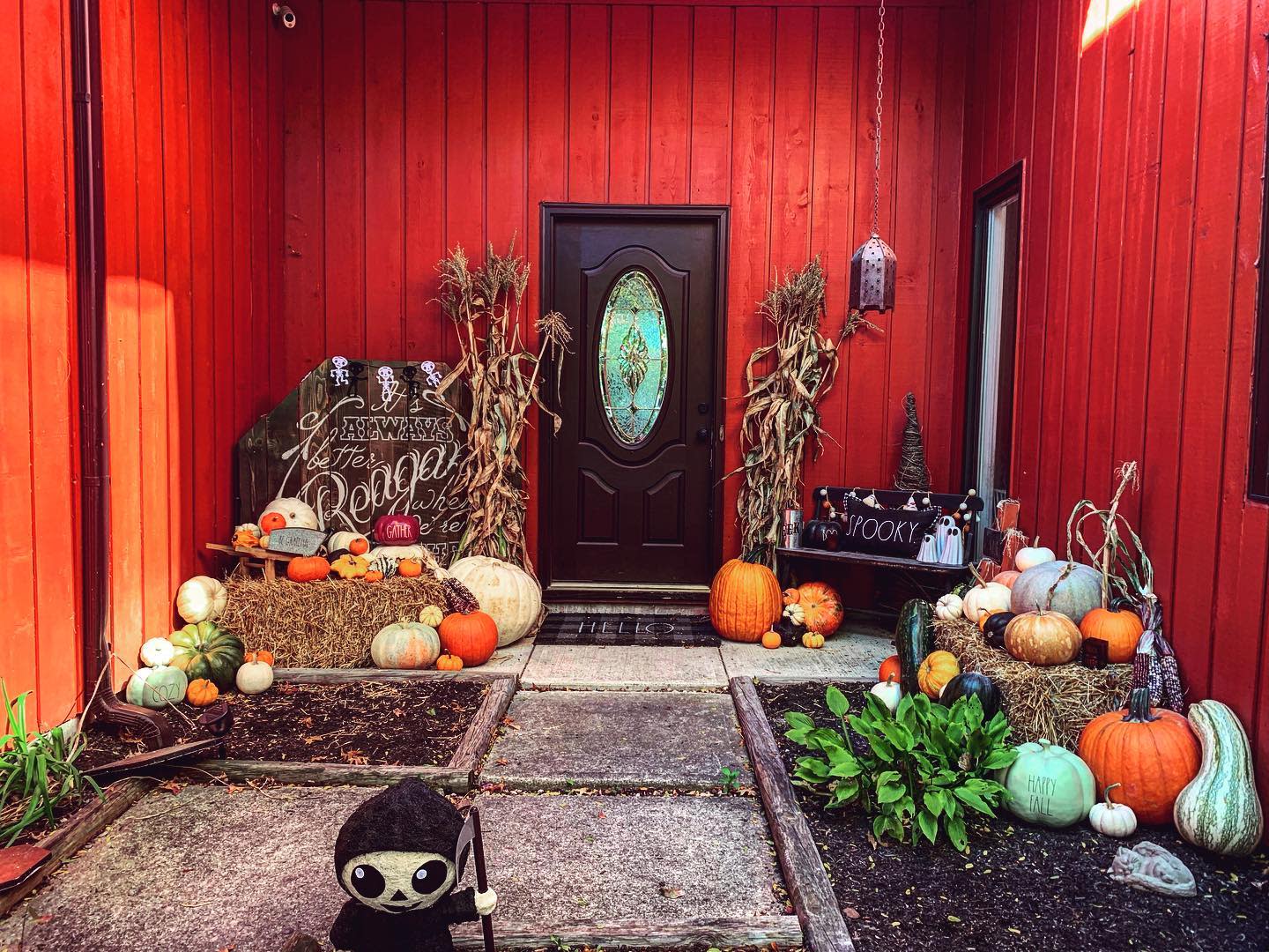 A front porch decorated for Halloween with pumpkins, hay bales, cornstalks, a "Reaper" sign, and a small Grim Reaper figure