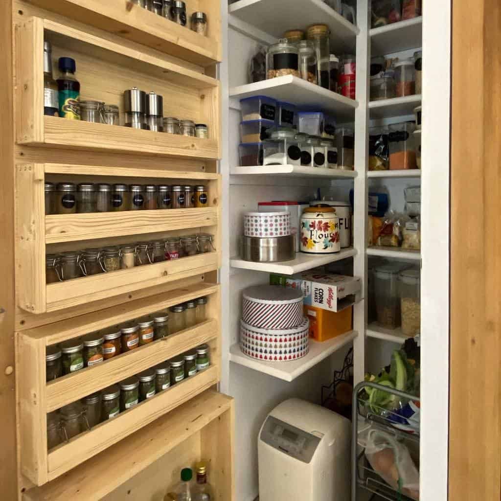 A neatly organized pantry with spice racks on the door and shelves stocked with jars, tins, and a variety of food items