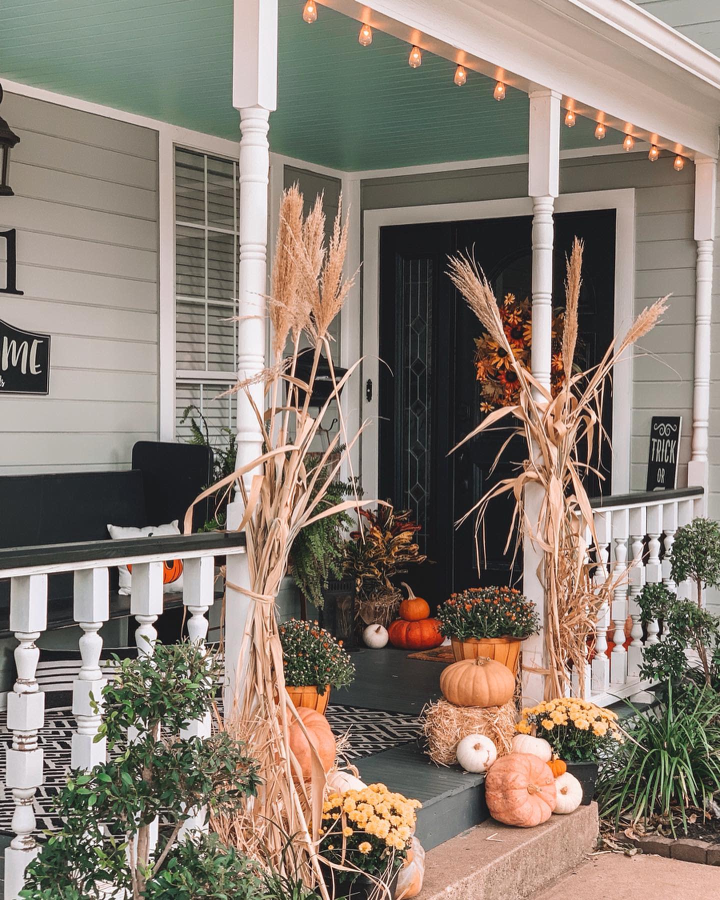 Charming fall porch decorated with pumpkins, mums, cornstalks, and warm string lights, creating a cozy autumn entrance