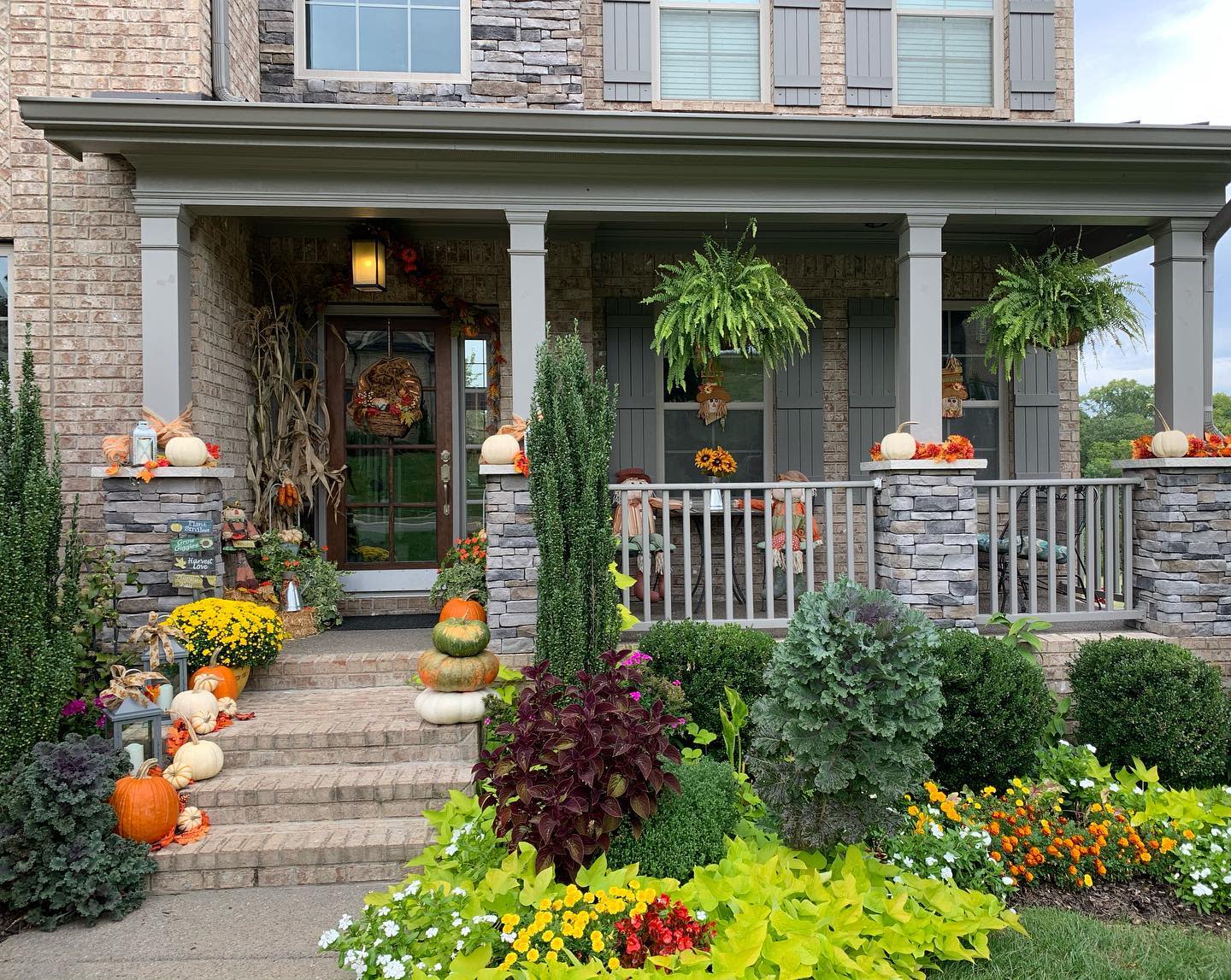 Cozy porch decorated with pumpkins, flowers, and greenery for fall; wreath on door and vibrant garden in front