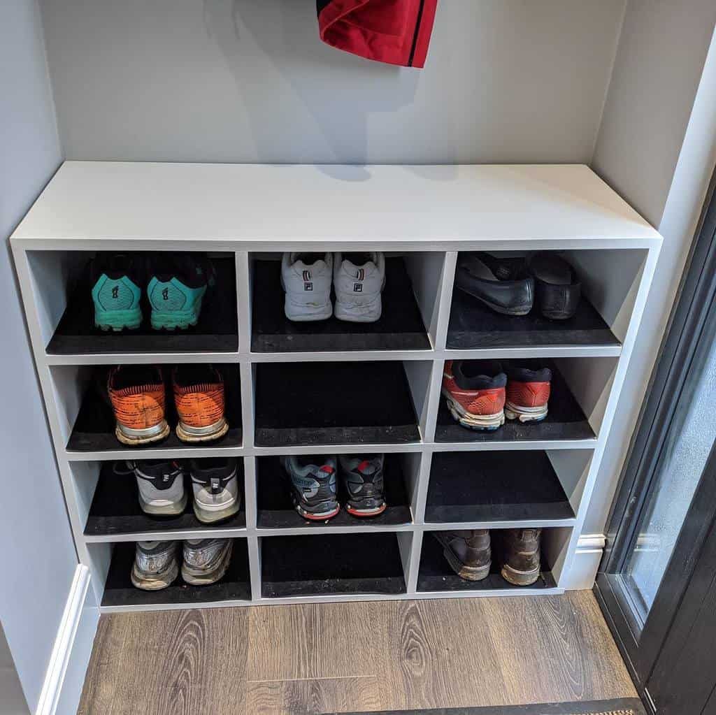 A white cubby shoe rack with ten pairs of shoes, including sneakers and boots, organized neatly in a white room with a wooden floor