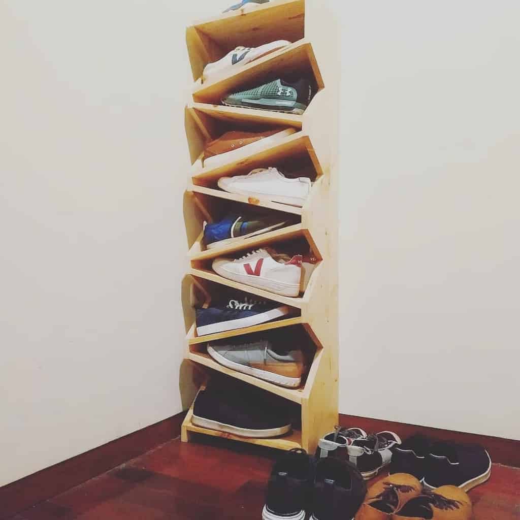 A vertical wooden shoe rack with multiple shelves stands in a corner, holding various sneakers