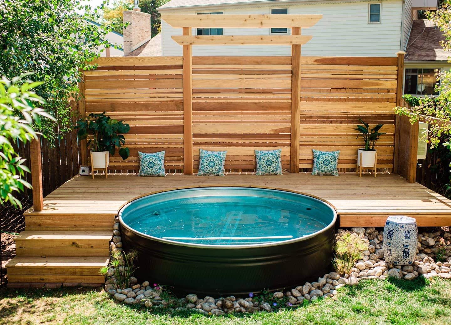 Stylish backyard with a stock tank pool, wooden deck, slatted privacy fence, blue accent pillows, and potted plants for a serene retreat