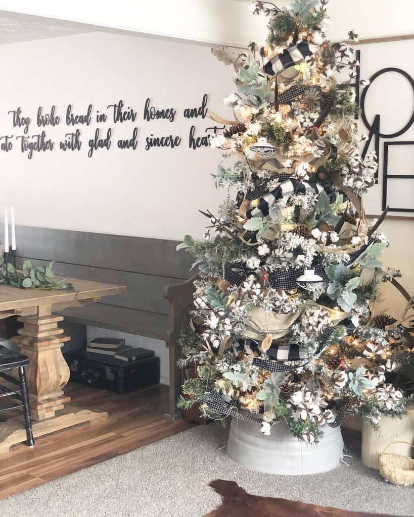 A decorated Christmas tree with white lights and ribbons stands in a cozy living room with a wall quote in the background