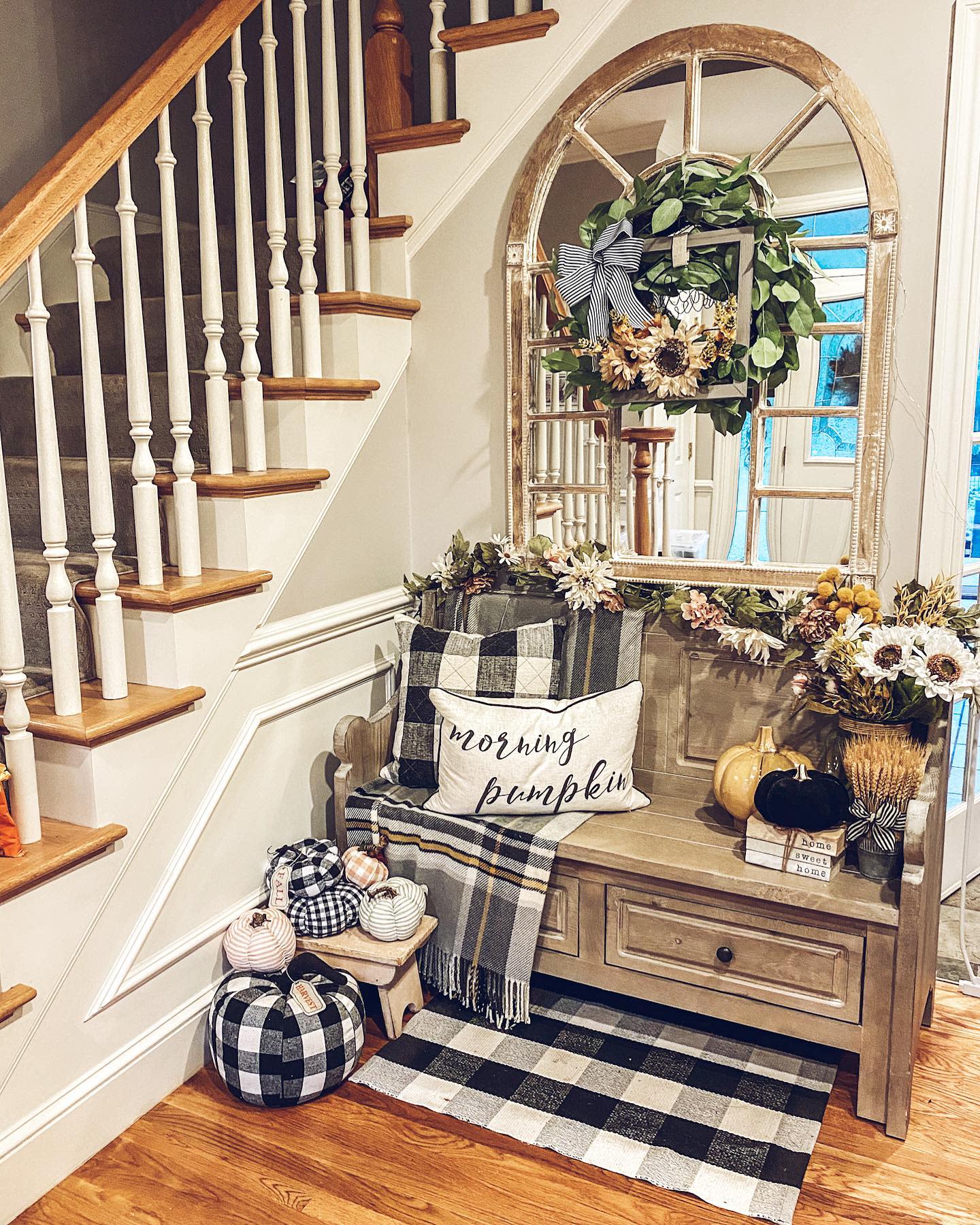 Cozy autumn-themed entryway with checkered pumpkins, a "morning pumpkin" pillow, and a decorative wreath on a large mirror