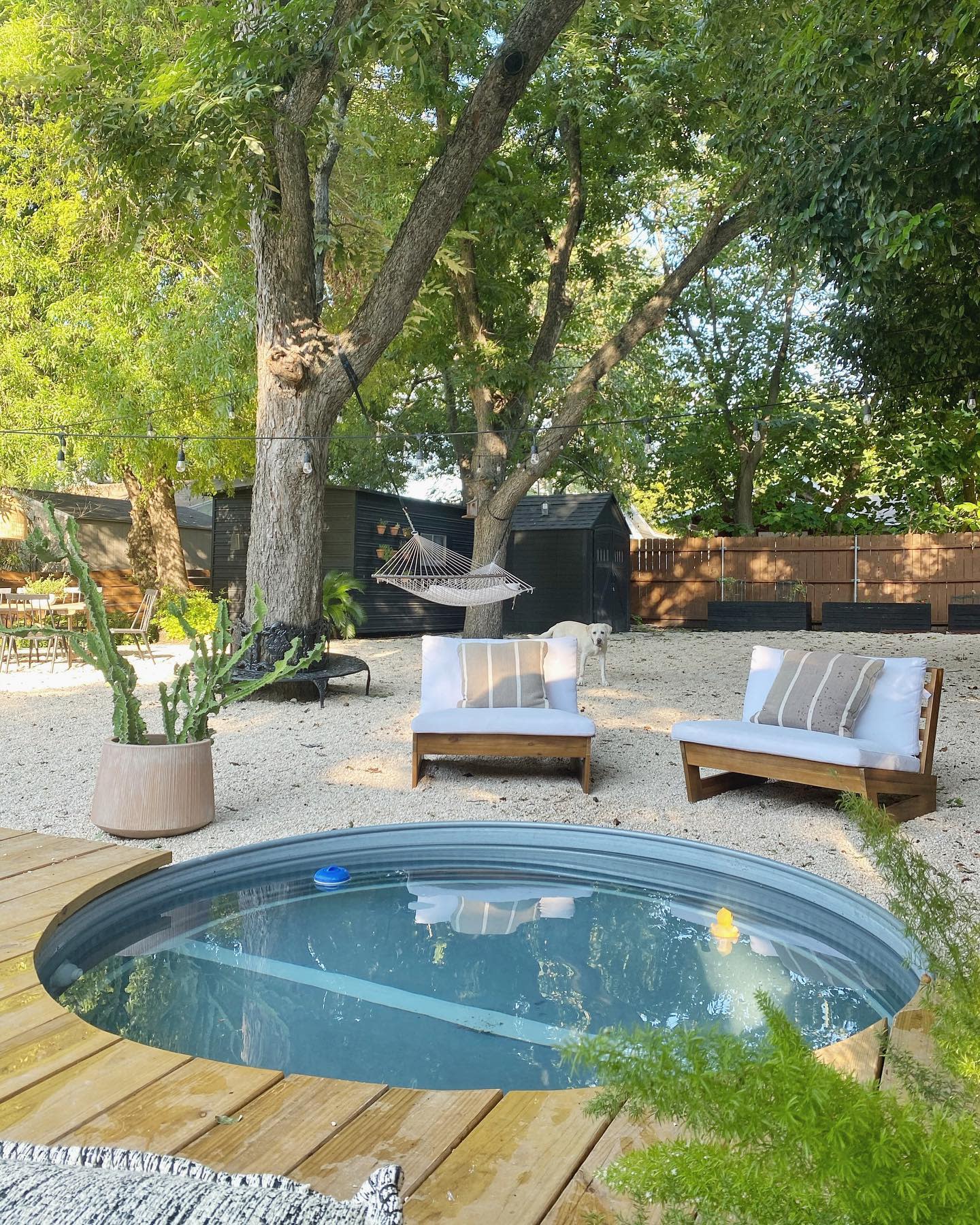 Tranquil backyard with a sunken stock tank pool, wooden deck, cozy seating, hammock, string lights, and lush greenery for relaxation