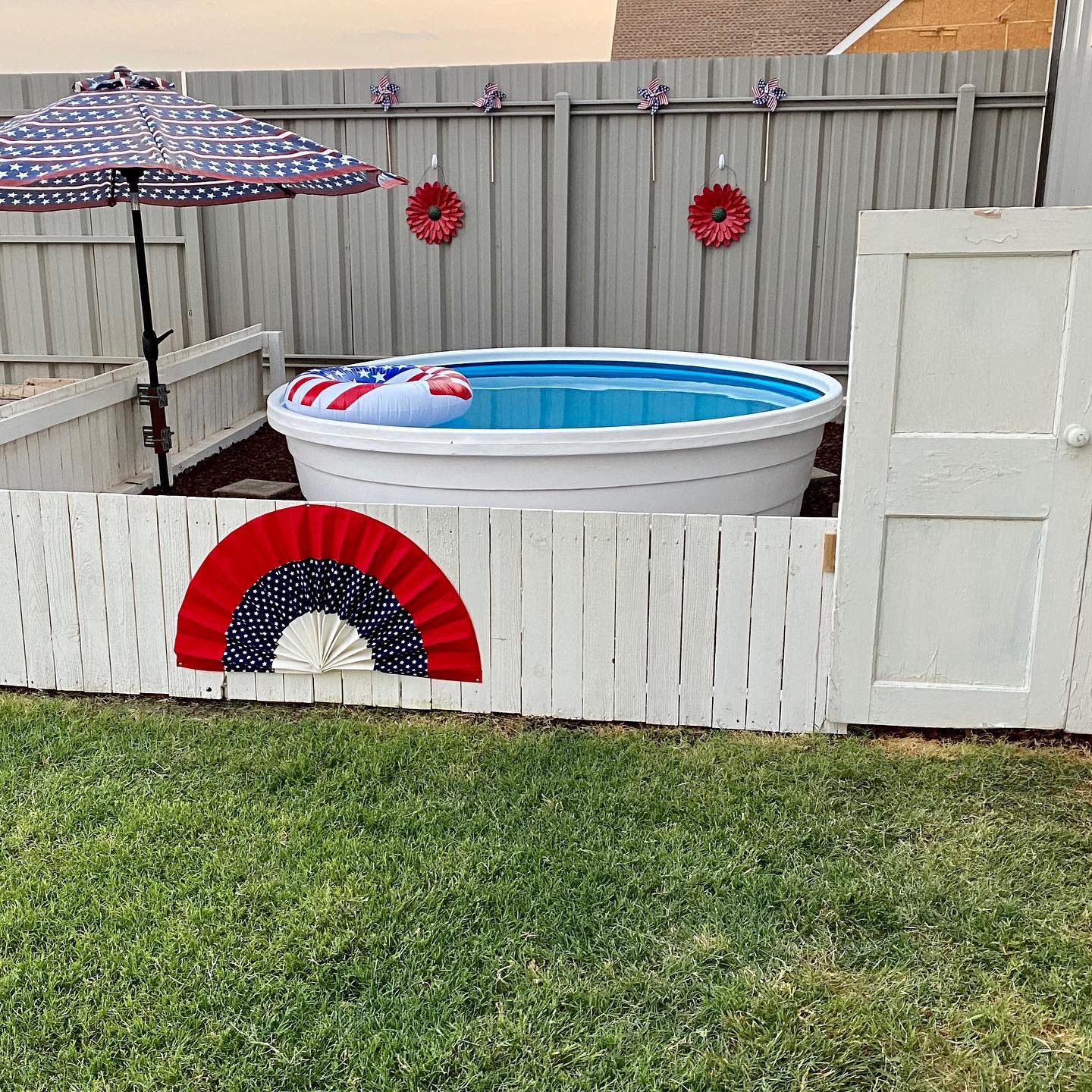 Small round pool with a patriotic-themed float and umbrella in a fenced yard featuring red star decorations on the fence