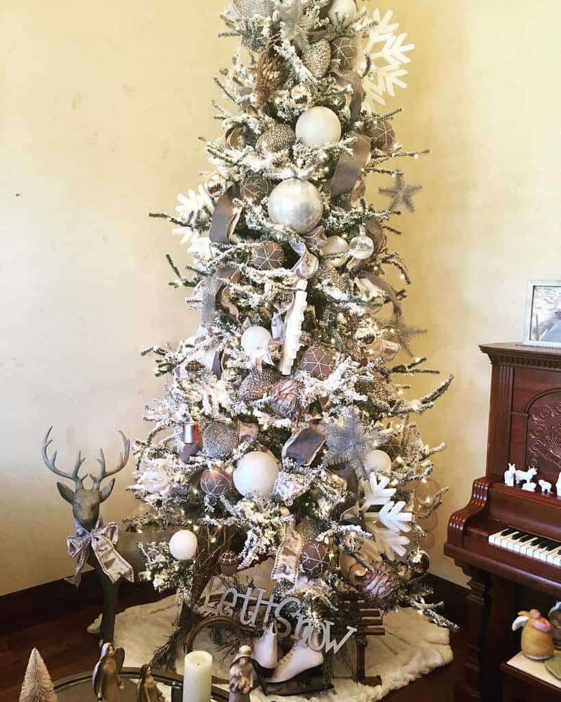 A Christmas tree with white and silver decorations, surrounded by ornaments and a piano in the background