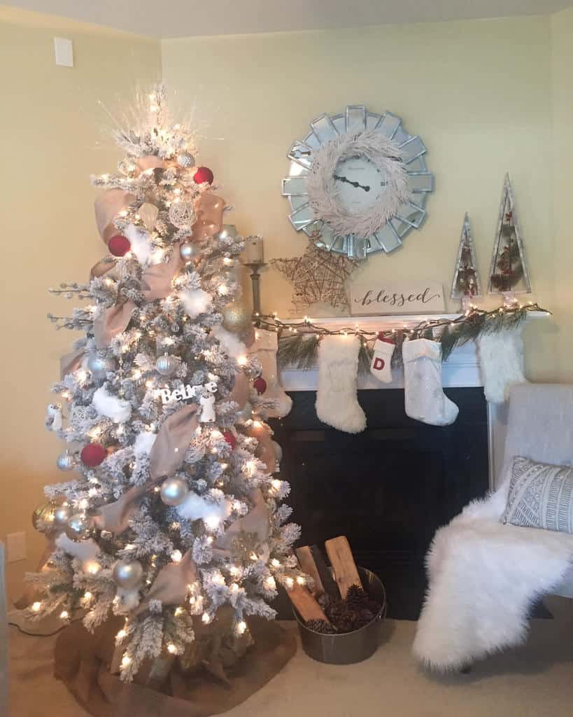 A decorated Christmas tree with white and gold ornaments near a fireplace with stockings, a mirror, and festive decorations