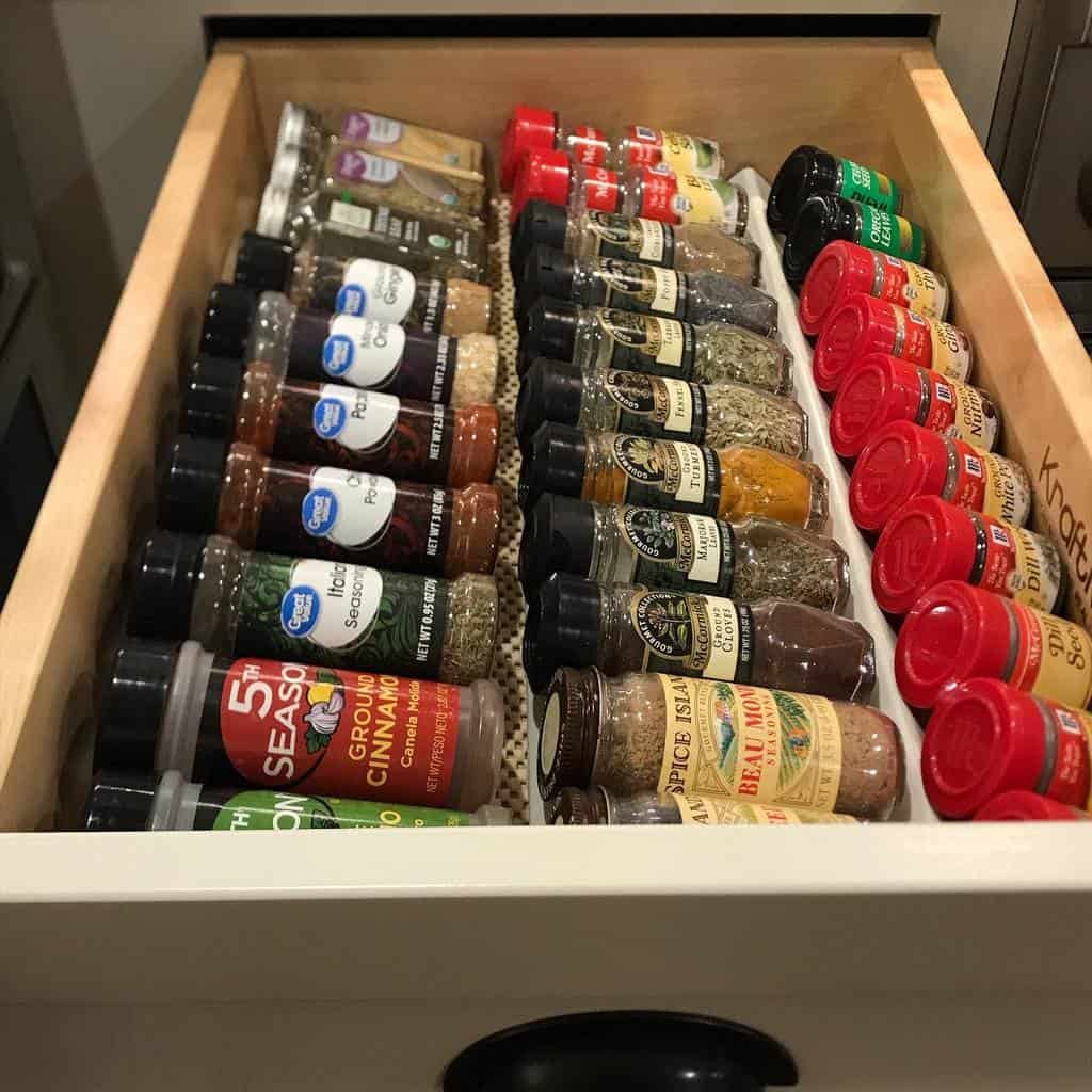 Open drawer with various spice jars neatly organized in two rows, including cinnamon, oregano, and paprika