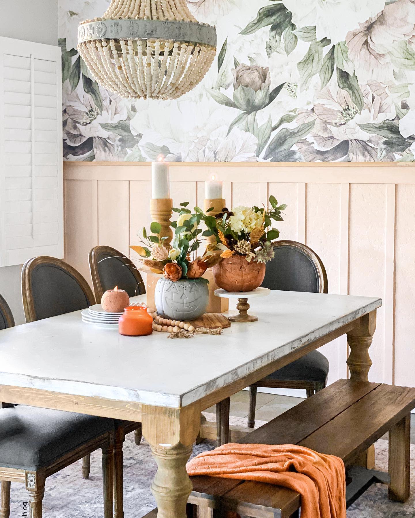 Dining table with floral decor, a beaded chandelier, and floral wallpaper in background