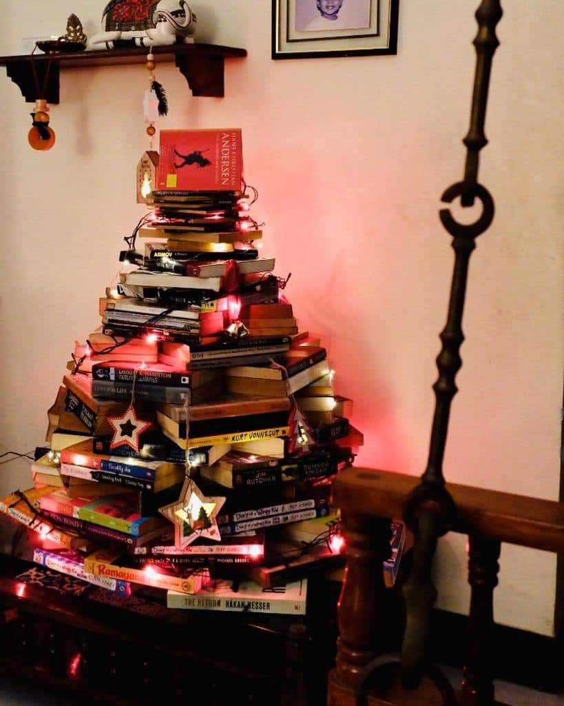 A Christmas tree made of stacked books, decorated with red lights and star ornaments