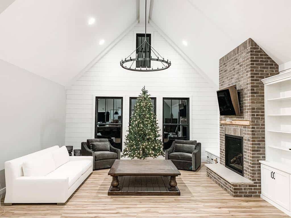 Spacious living room with a vaulted ceiling, Christmas tree, white sofa, dark armchairs, and a brick fireplace with a TV above