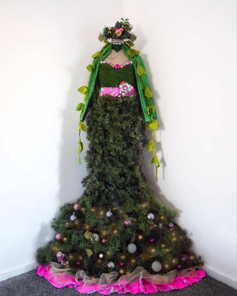 A mannequin draped in a dress made of Christmas tree foliage and ornaments, with a pink flower belt and veil