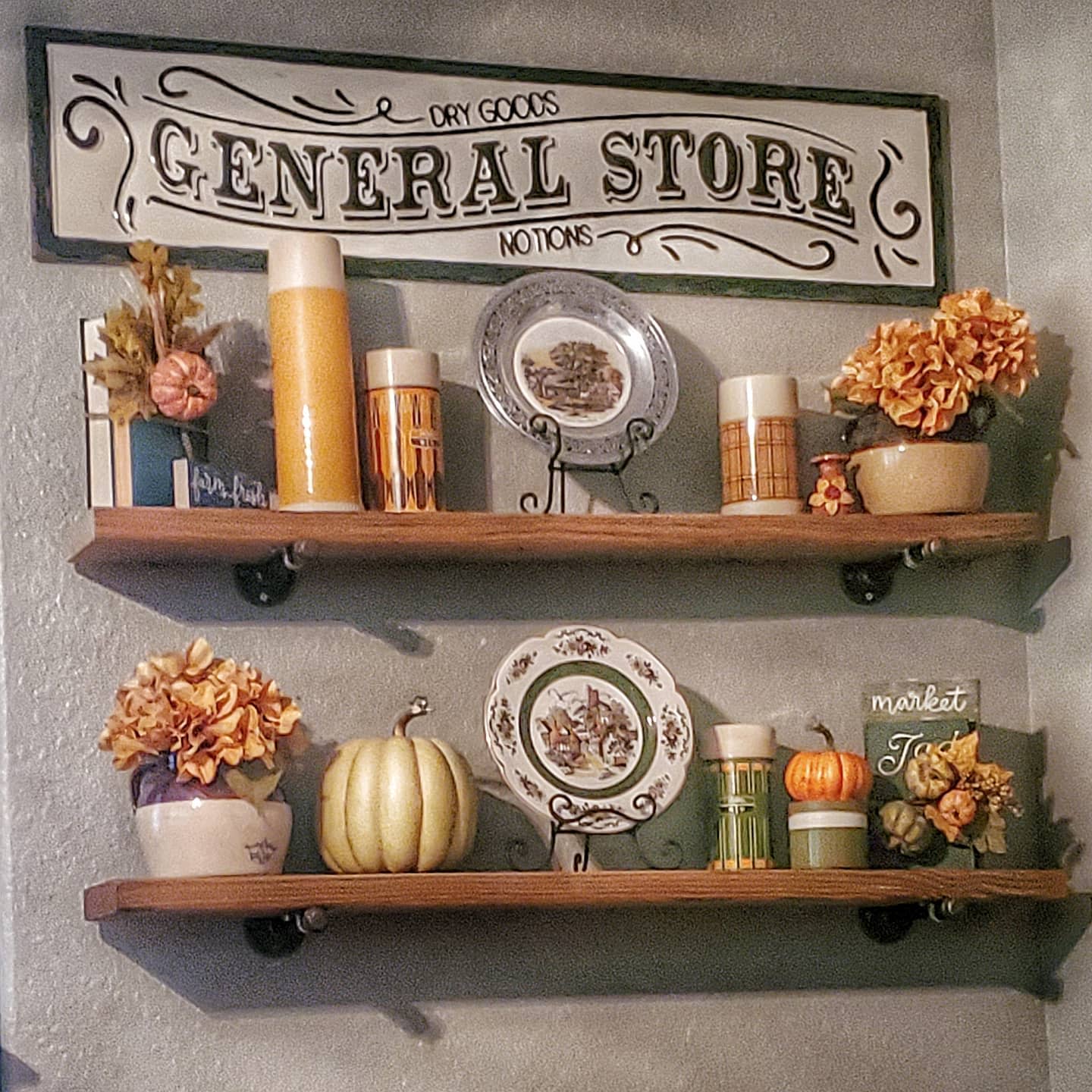 Two wooden shelves with autumn-themed decor, including pumpkins, flowers, candles, and plates with a "General Store" sign above