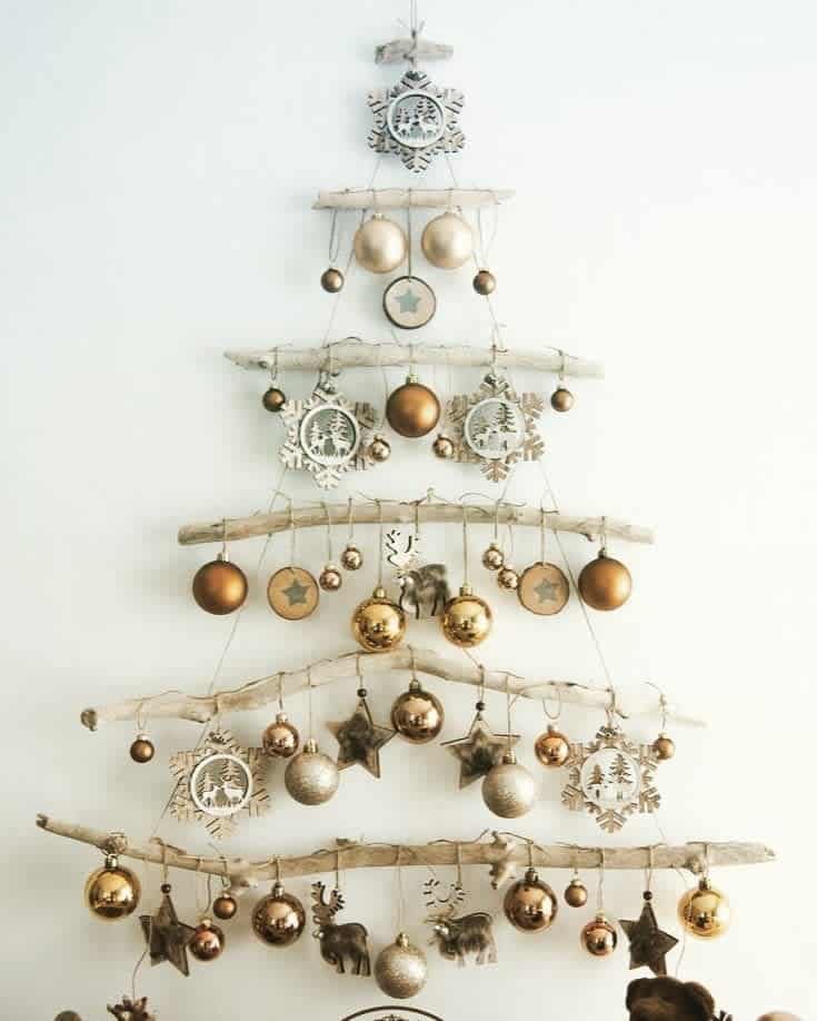 Minimalist Christmas tree made from branches, adorned with gold and silver ornaments, star shapes, and wooden decorations