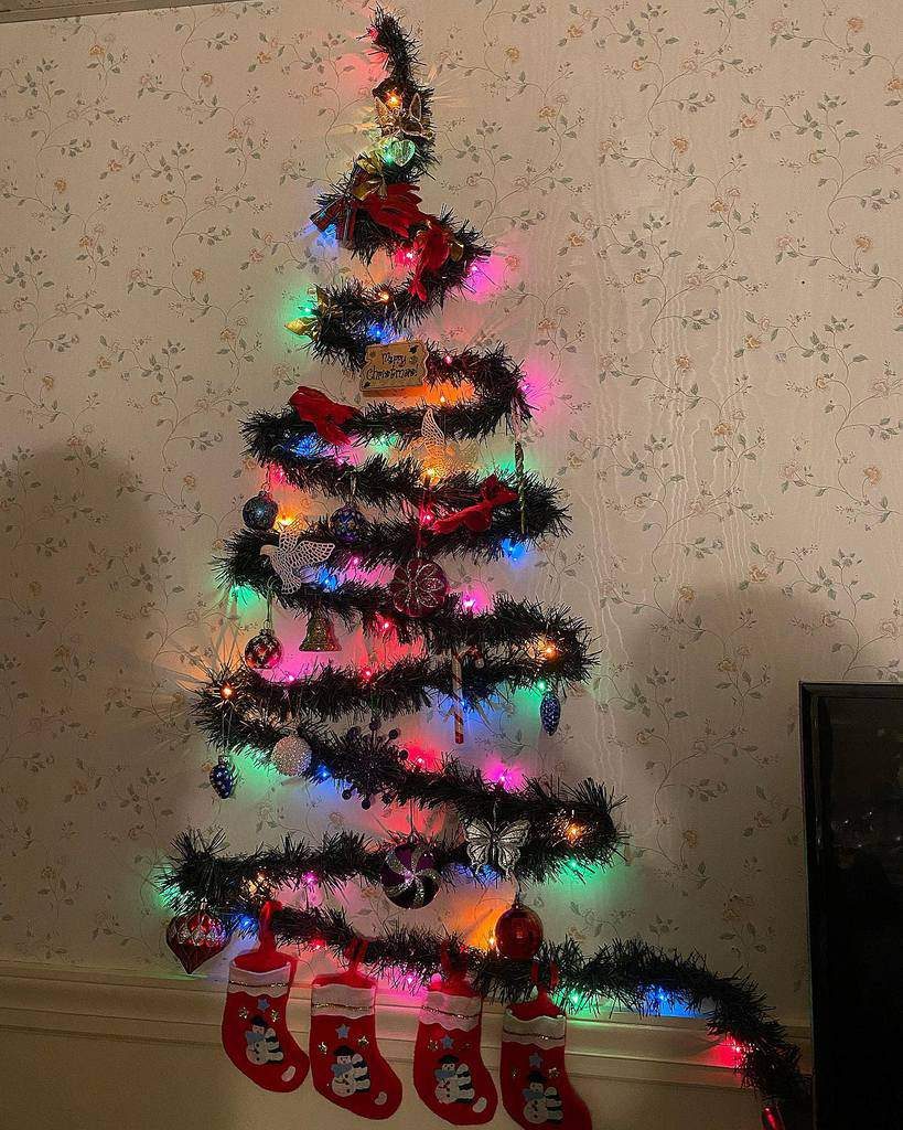 Wall-mounted Christmas tree with colorful lights and ornaments, featuring four red stockings hanging at the bottom