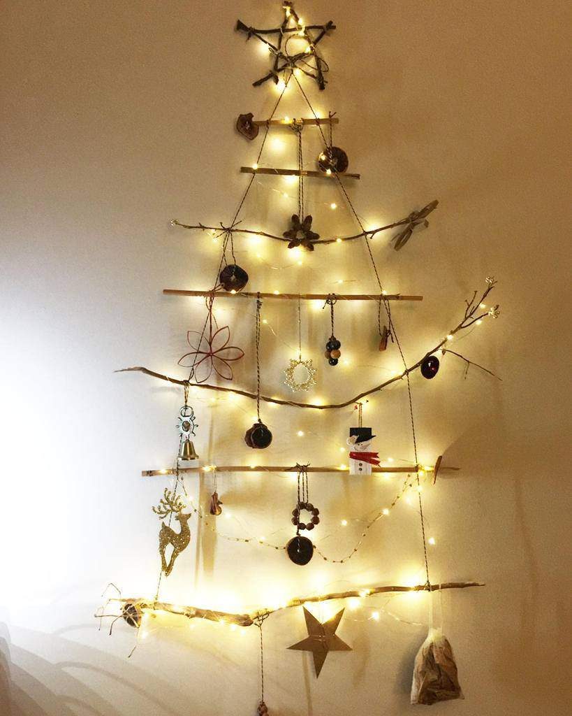 Minimalist Christmas tree wall hanging made of sticks, adorned with lights, stars, and ornaments, forming the shape of a tree