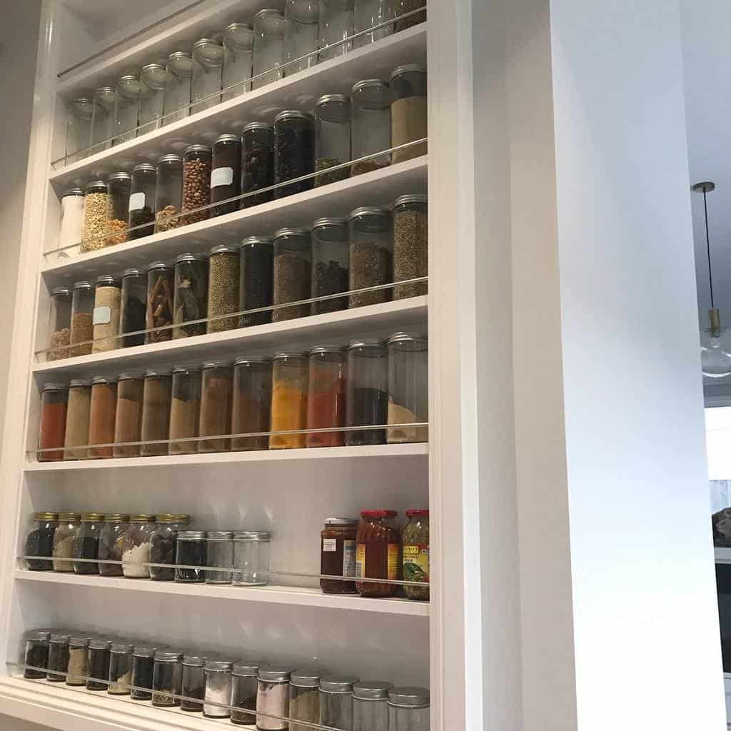 Wall-mounted spice rack with multiple shelves holding jars of spices, herbs, and condiments in a kitchen setting