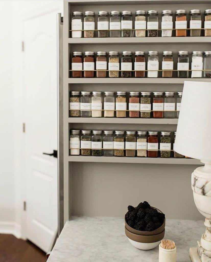 Sleek built-in spice rack with labeled glass jars, neatly organized on open shelves in a neutral-toned kitchen