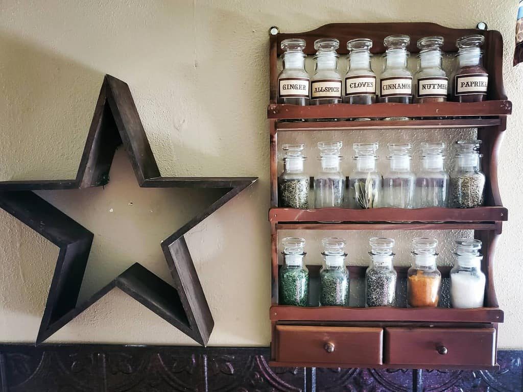 Rustic wooden spice rack with labeled glass jars and small drawers, adding charm to a vintage-style kitchen wall with decorative accents