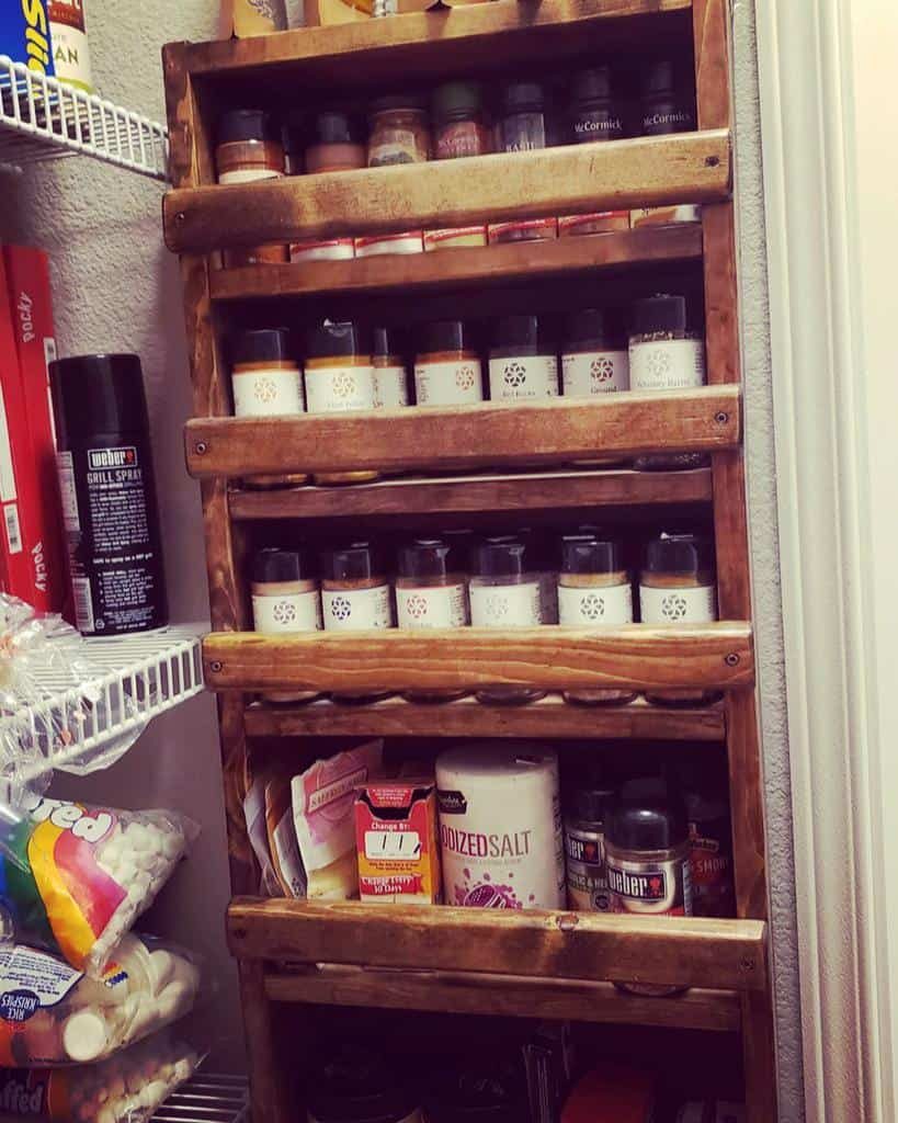 Wooden spice rack filled with assorted spices and seasonings; nearby pantry shelves store various food items like marshmallows and snacks