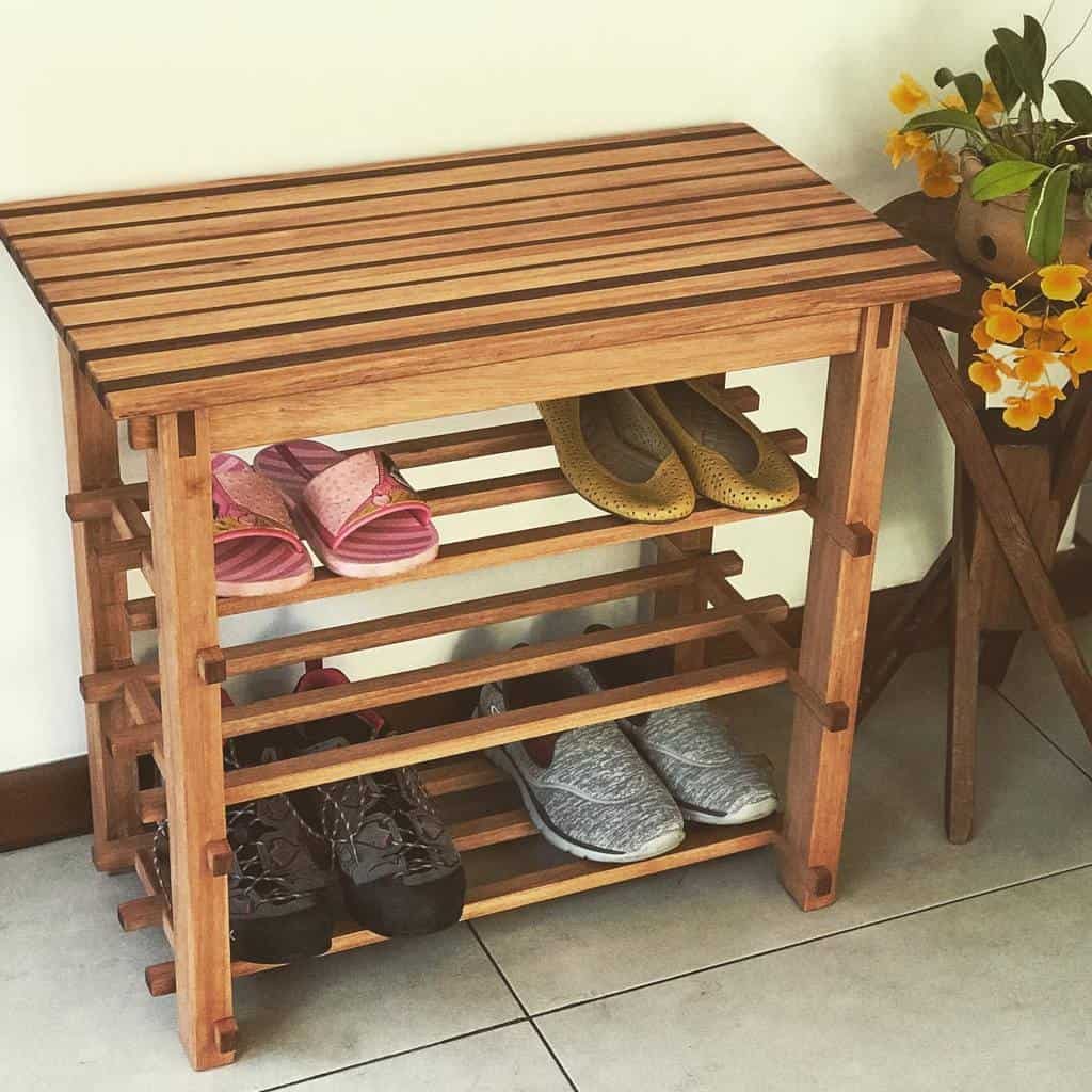 Wooden shoe rack with a slatted top and multiple shelves, neatly organizing various footwear in a cozy indoor corner