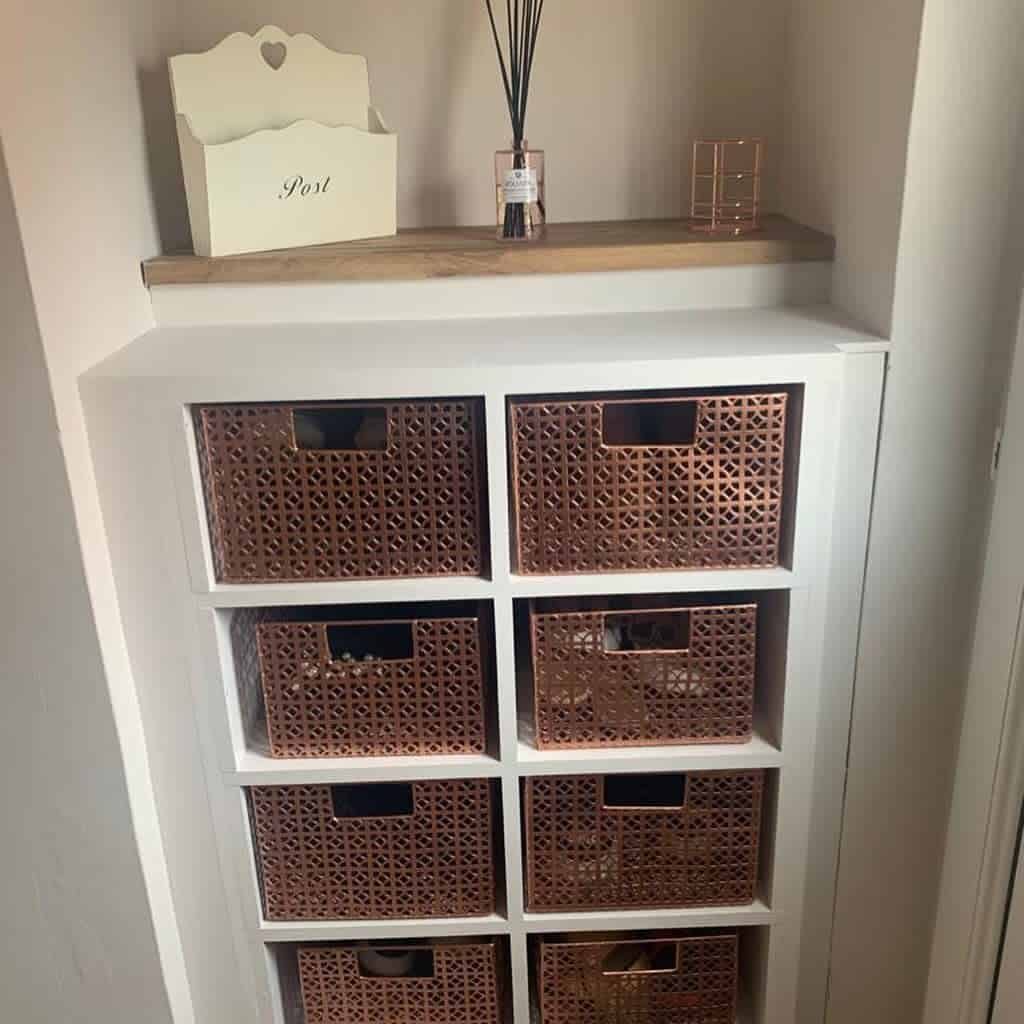 White shoe storage unit with woven copper baskets, neatly organized in a nook with a wooden top and decorative accents