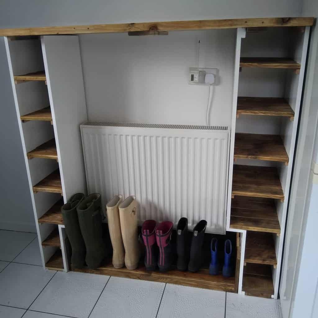 Custom-built wooden shoe storage with side shelves and a space for boots, designed around a radiator in a functional entryway