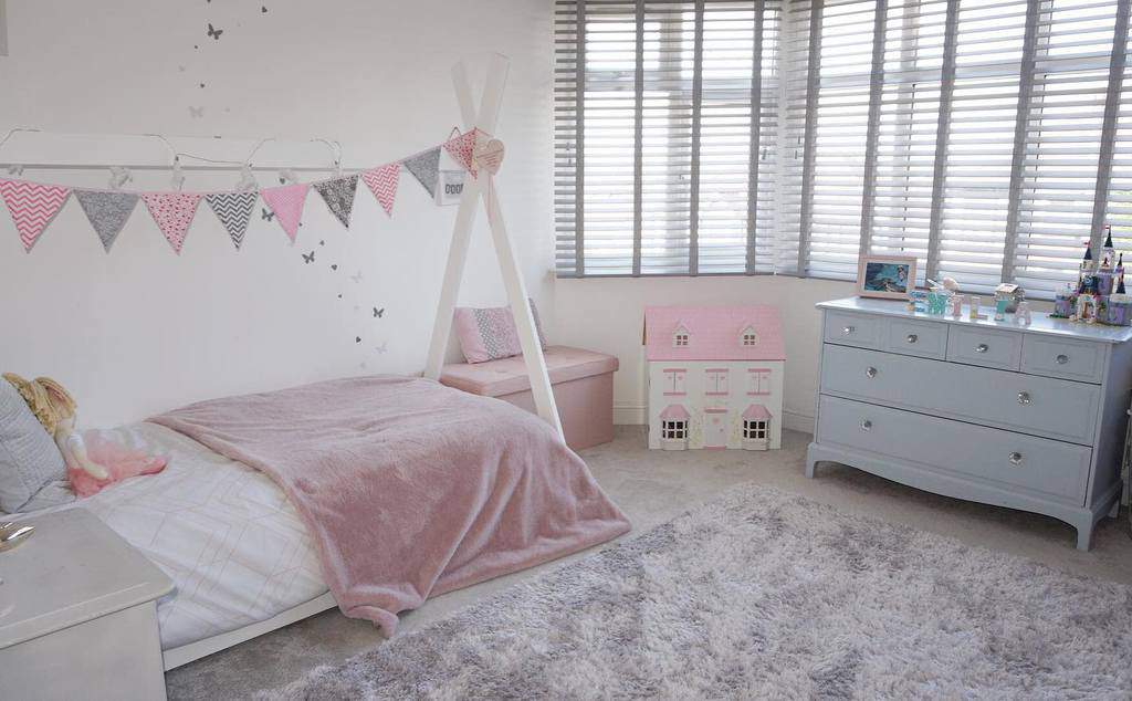 Charming girls' bedroom with a bay window, soft pink and pastel decor, a cozy bench seat, and playful bunting for a whimsical touch.