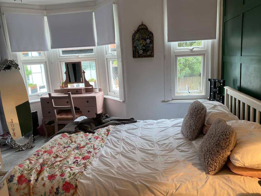 Cozy bedroom with a bay window, pink vanity, floral bedding, and a green accent wall, creating a charming and inviting space.